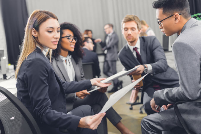 Group of people in business attire talking and sharing documents.