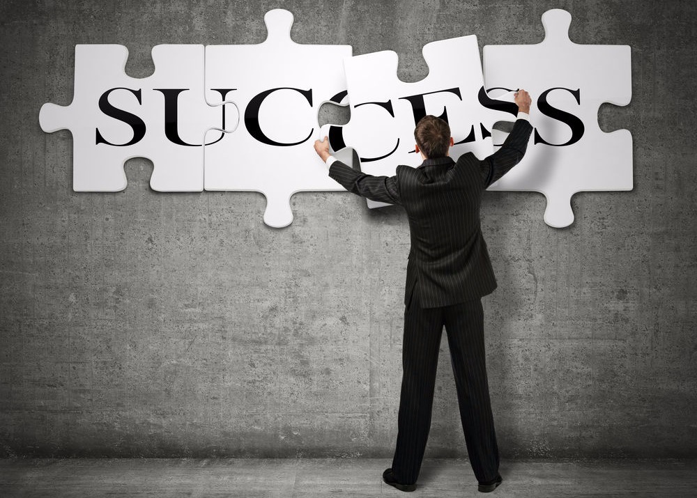 Image of a man standing in front of a jigsaw puzzle with the words success.